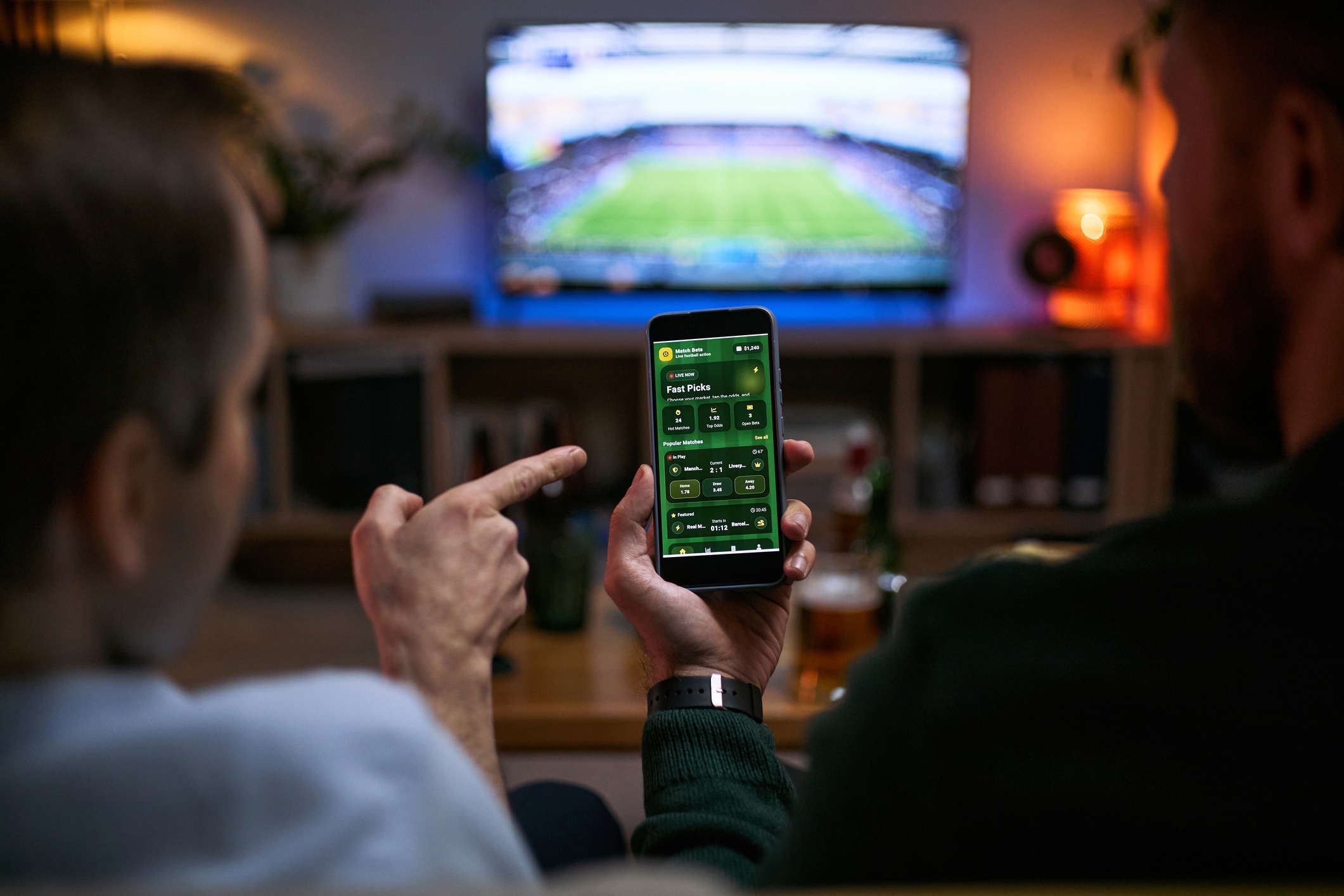 Young adult men watching football match and checking betting app on smartphone, expressing male friendship and shared leisure. Useful for sports betting, gaming, entertainment marketing