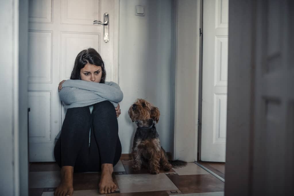 Woman with mental health problems is sitting desperate on the floor and crying and her dog is next to her