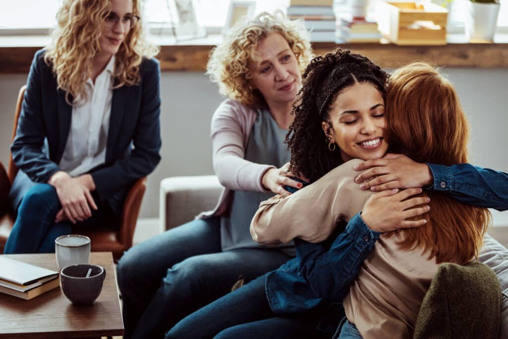 Group therapy members hugging while others offer support