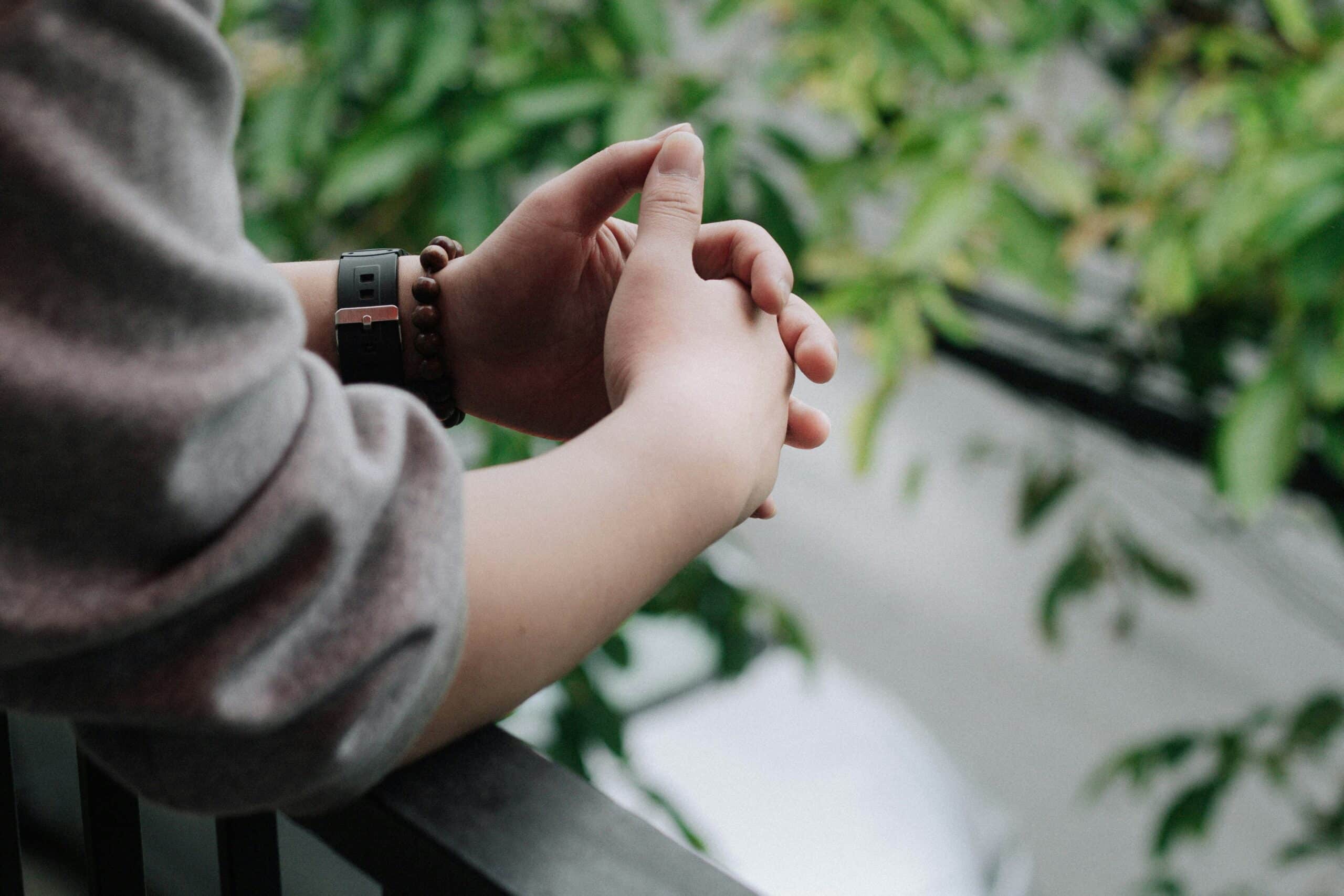 person in long sleeve gray shirt holding their hands together wearing brown beaded bracelet