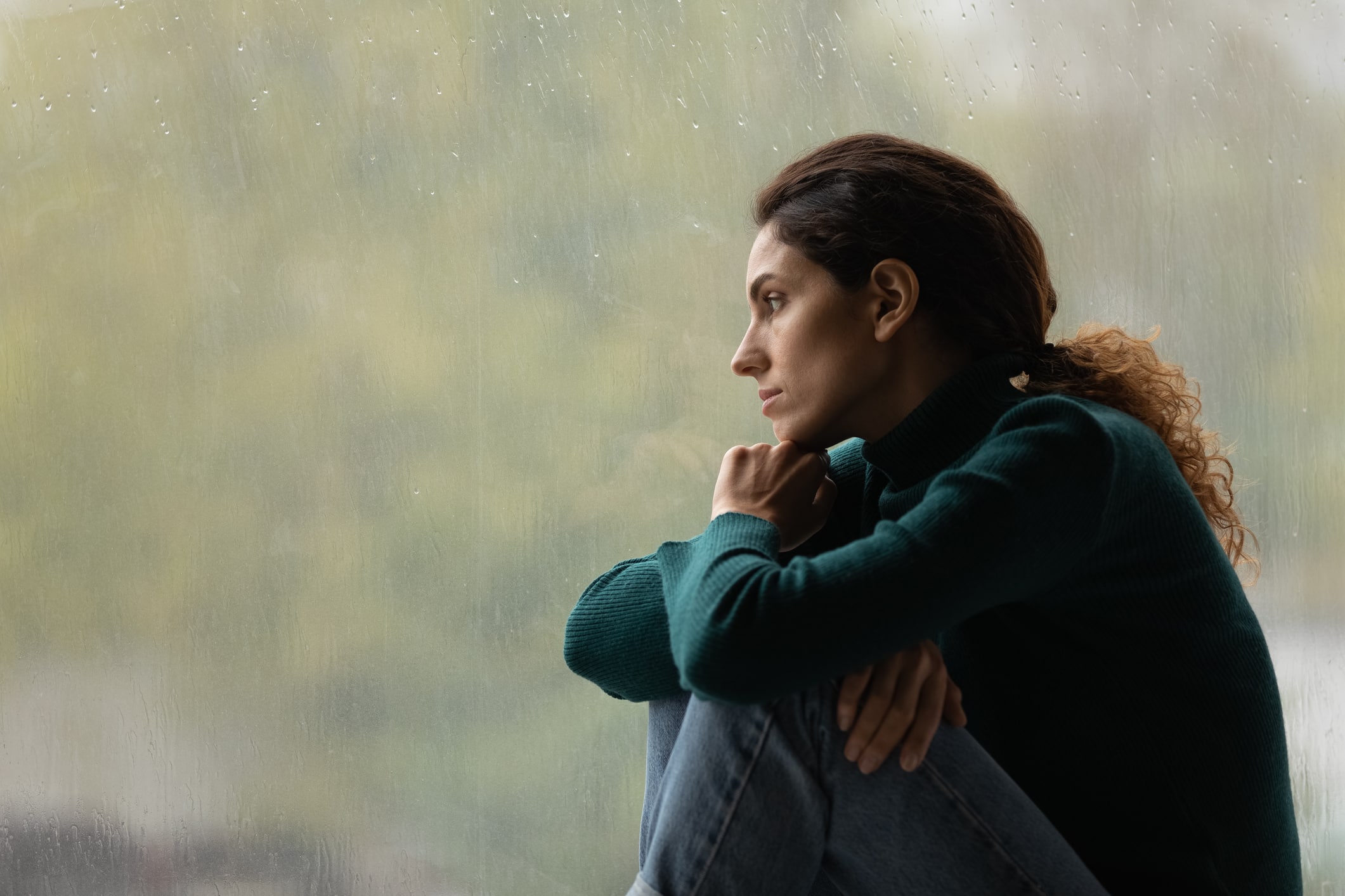 woman depressed looking out window clutching her legs