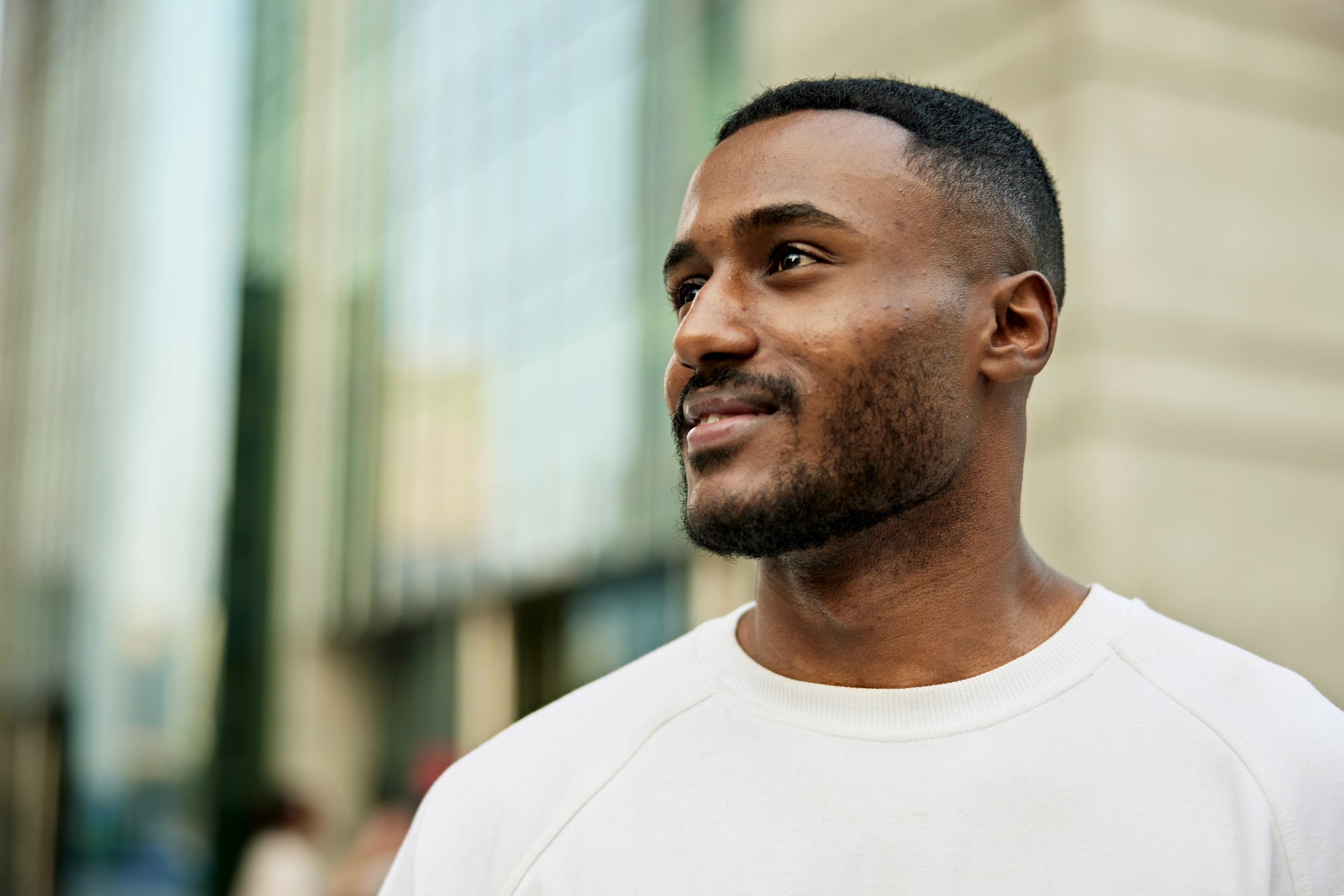 Headshot of casually dressed professional standing outdoors in plaza, looking away with slight smile.